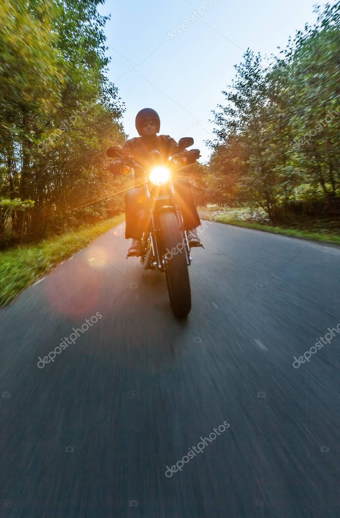 Dark motorbiker riding high power motorbike in nature with beautiful sunrise light