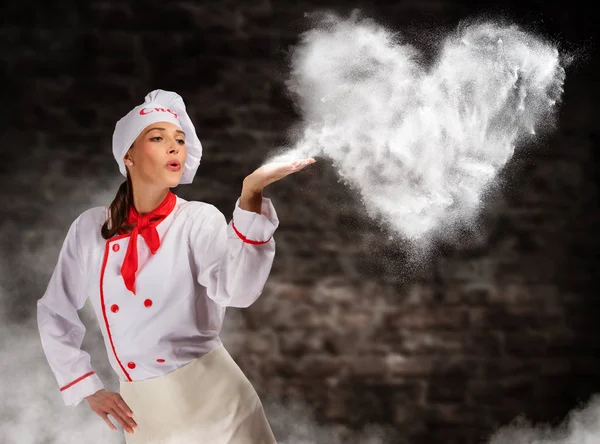 Attractive young woman in kitchen blowing the heart shape made of flour — Stock Photo, Image