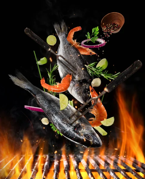 Flying raw whole bream fish and prawns with ingredients above grill fire — Stock Photo, Image