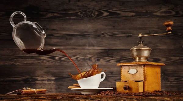 Liquide éclaboussant de café de la cruche dans la tasse sur la table en bois — Photo
