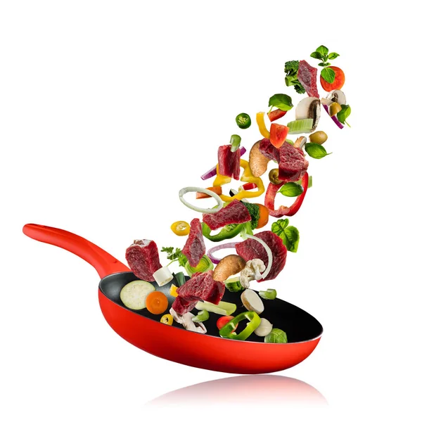 Fresh vegetables and beef meat flying into a pan on white background