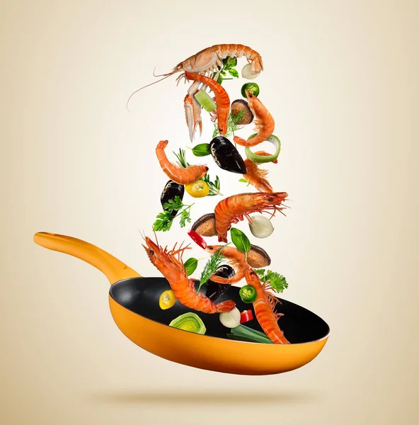 Fresh sea food and vegetables flying into a pan on brown background — Stock Photo, Image