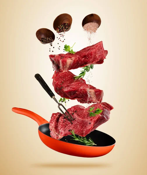 Flying raw steaks with cooking ingredients from pan — Stock Photo, Image