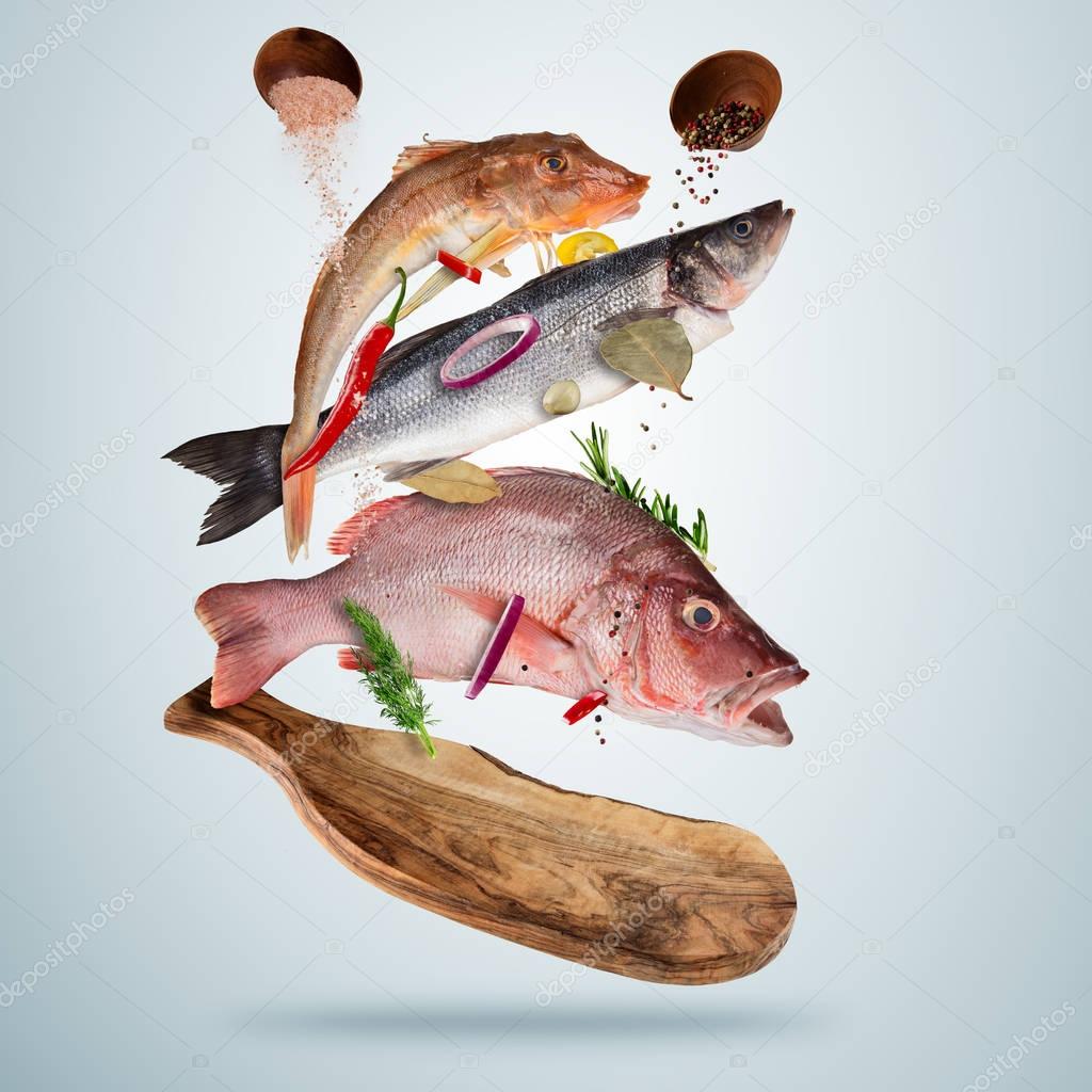 Fresh sea fish with falling spices, flying above wooden board