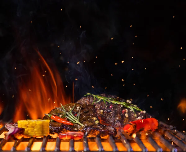 Beef steaks on the grill grate, flames on background — Stock Photo, Image