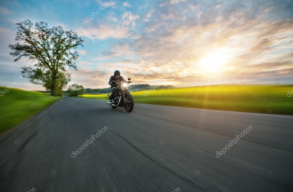 Dark motorbiker riding high power motorbike in nature with beautiful sunset light. Travel and transportation. Freedom of motorbike riding