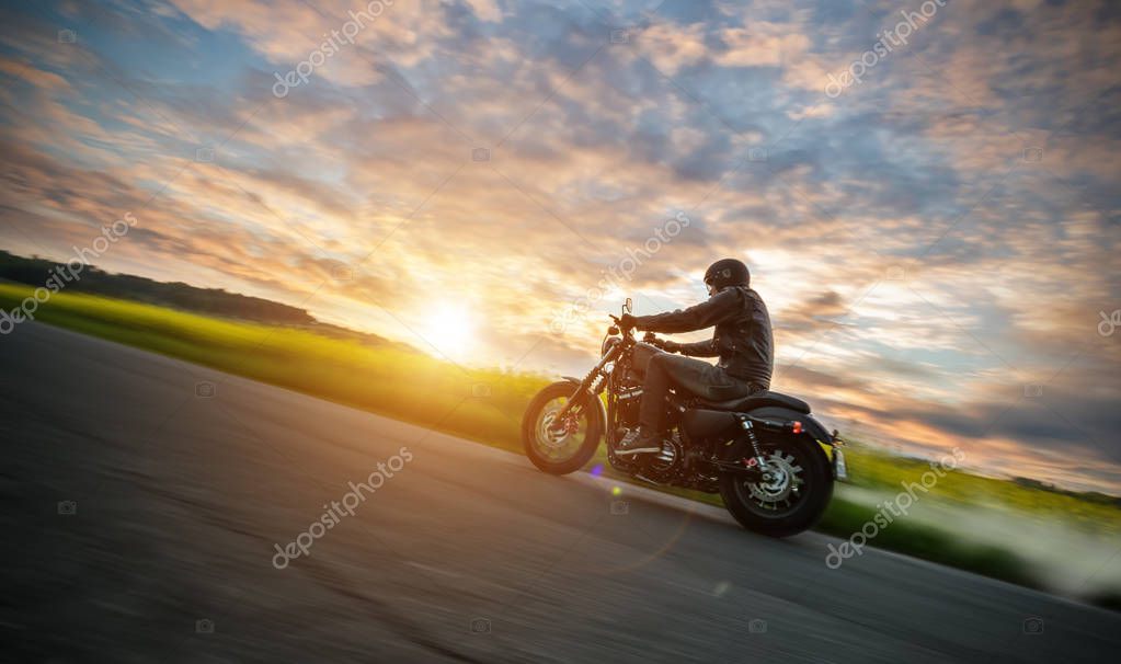 Dark motorbiker riding high power motorbike in nature with beautiful sunset light. Travel and transportation. Freedom of motorbike riding
