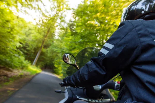 Close-up of motorbiker riding on empty road in forest — Stock Photo, Image