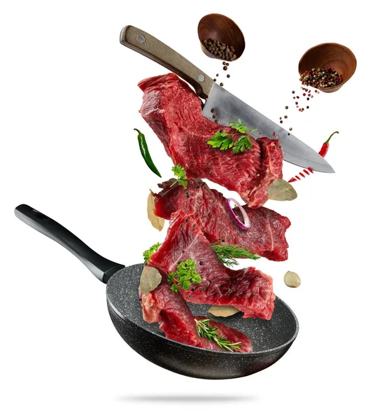 Flying raw steaks with cooking ingredients from pan — Stock Photo, Image