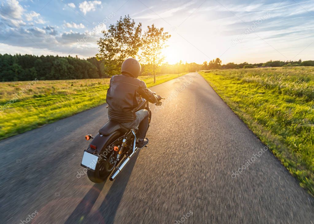 Dark motorbiker riding high power motorbike in nature with beautiful sunset light. Travel and transportation. Freedom of motorbike riding