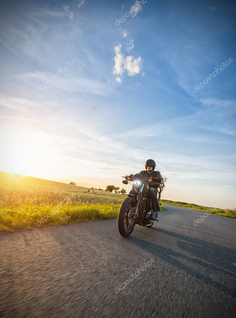 Dark motorbiker riding high power motorbike in nature with beautiful sunset light. Travel and transportation. Freedom of motorbike riding