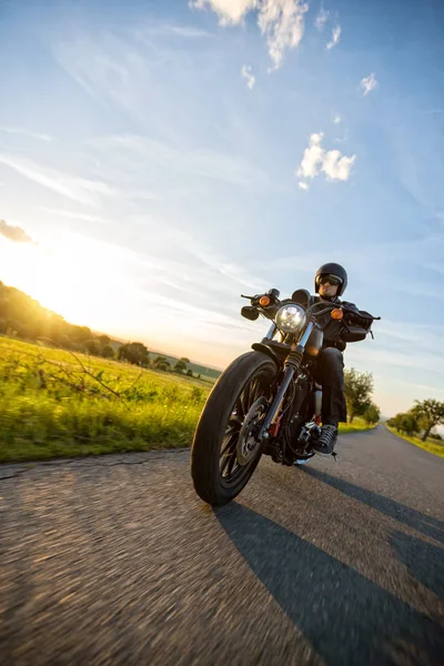 Motociclista escuro montando moto de alta potência no pôr do sol — Fotografia de Stock