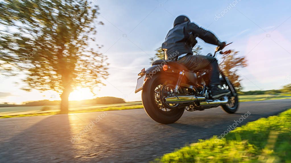 Dark motorbiker riding high power motorbike in nature with beautiful sunset light. Travel and transportation. Freedom of motorbike riding