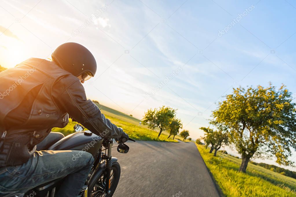 Dark motorbiker riding high power motorbike in nature with beautiful sunset light. Travel and transportation. Freedom of motorbike riding