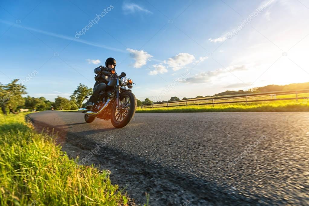 Dark motorbiker riding high power motorbike in nature with beautiful sunset light. Travel and transportation. Freedom of motorbike riding