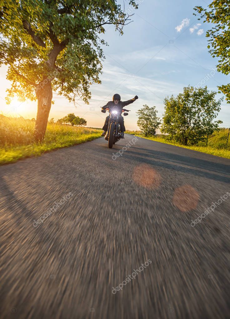 Dark motorbiker riding high power motorbike in nature with beautiful sunset light. Travel and transportation. Freedom of motorbike riding