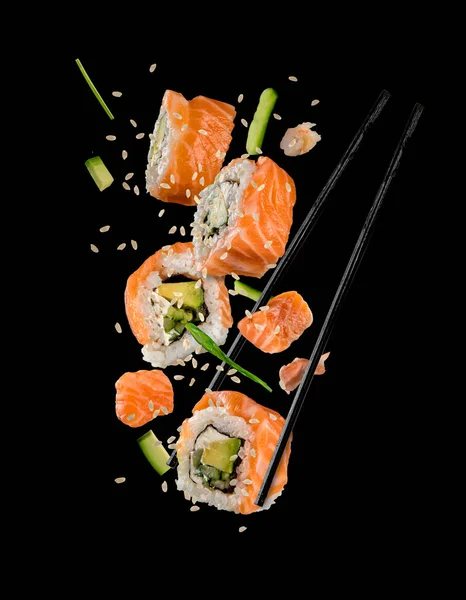 Sushi-Stücke zwischen Essstäbchen auf schwarzem Hintergrund — Stockfoto