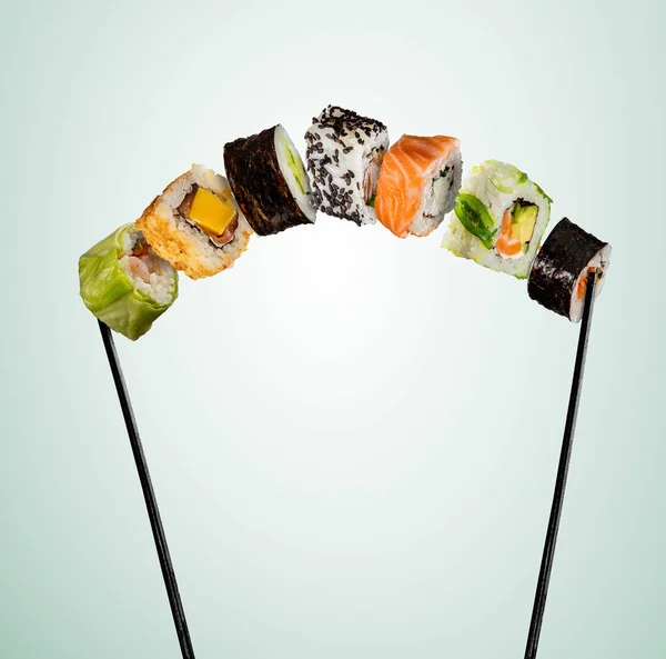 Sushi pieces placed between chopsticks on soft background — Stock Photo, Image