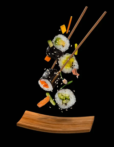 Σούσι κομμάτια τοποθετούνται μεταξύ chopsticks σε μαύρο φόντο — Φωτογραφία Αρχείου