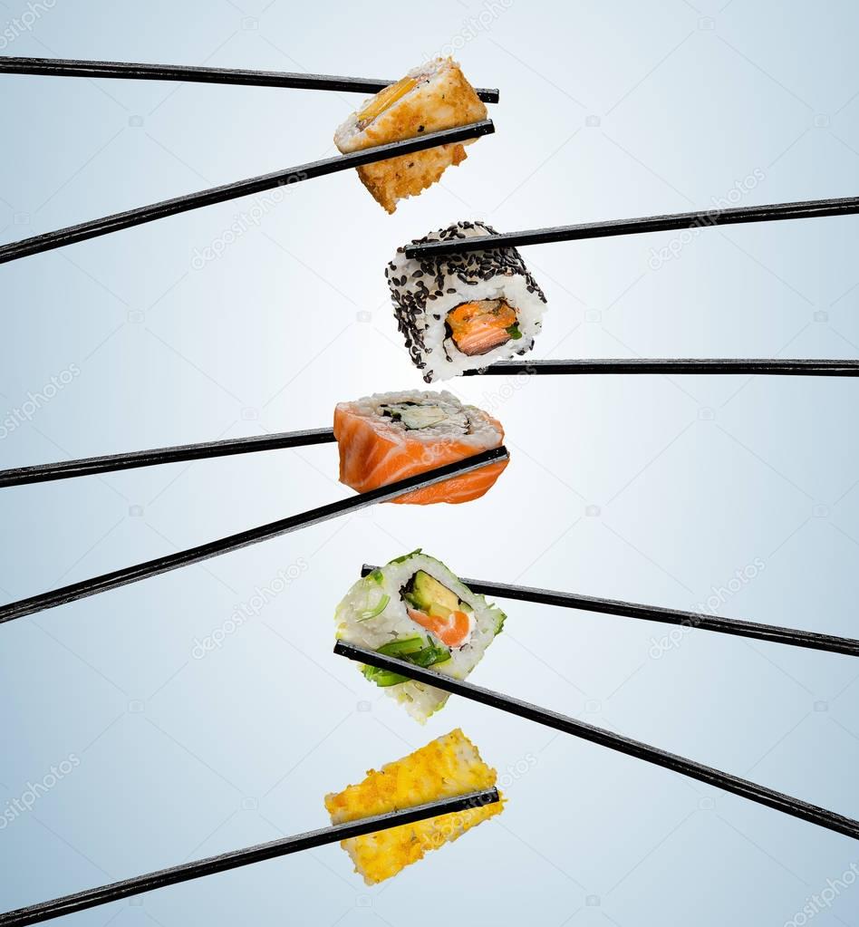Sushi pieces placed between chopsticks, on soft background