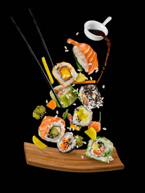 Sushi pieces placed between chopsticks on black background clipart