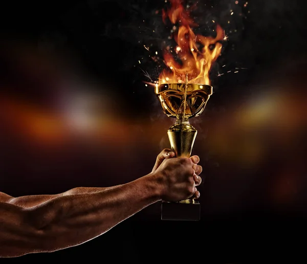 Muscular man arm holding burning trophy cup on black background — Stock Photo, Image