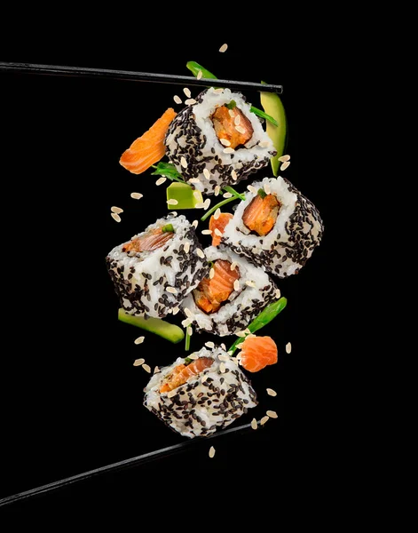 Piezas de sushi colocadas entre palillos sobre fondo negro — Foto de Stock