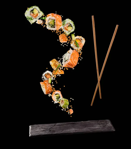 Trozos voladores de sushi con palillos de madera y plato de piedra, i — Foto de Stock