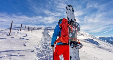 Kar ayakkabılarını toz karda yürürken snowboarder.
