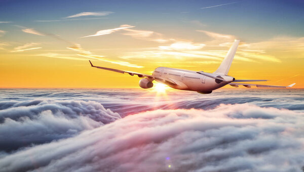 Big commercial airplane flying above clouds in sunset