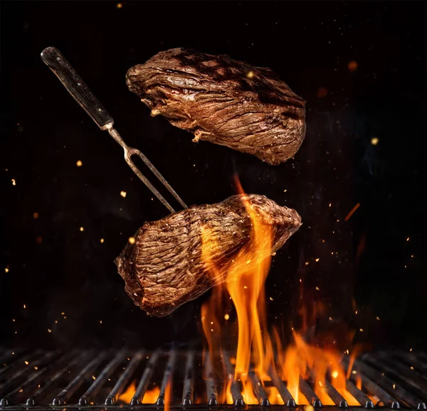 Flygande nötköttsbiffar över grill rutnät, isolerad på svart bakgrund — Stockfoto