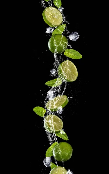 Slices of lime falling in water splash on black background — Stock Photo, Image