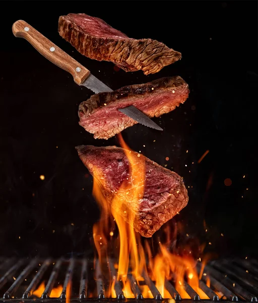 Flying pieces of beef steaks from grill grid on black background — Stock Photo, Image