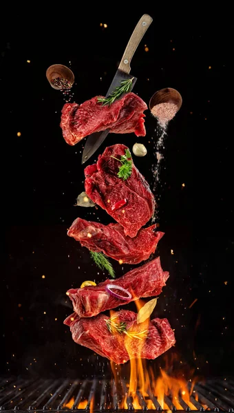 Літаючі шматки сирих яловичих стейків з сітки гриля на чорному фоні — стокове фото