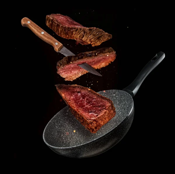 Flying pieces of beef steaks from pan on black background — Stock Photo, Image