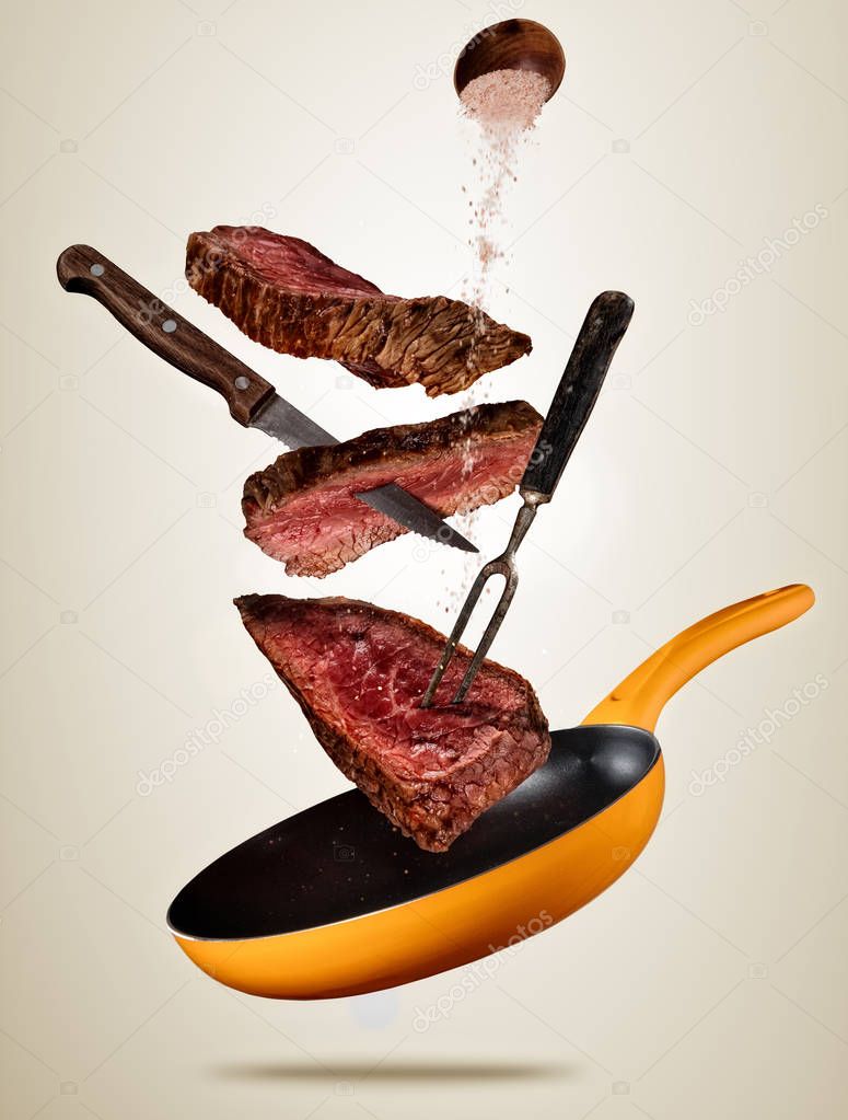 Flying pieces of beef steaks from pan on colored background.