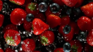 Çilekleri su sıçratan süper yavaş çekimde, siyah arka planda. Yüksek hızlı sinema kamerası, 1000 fps..