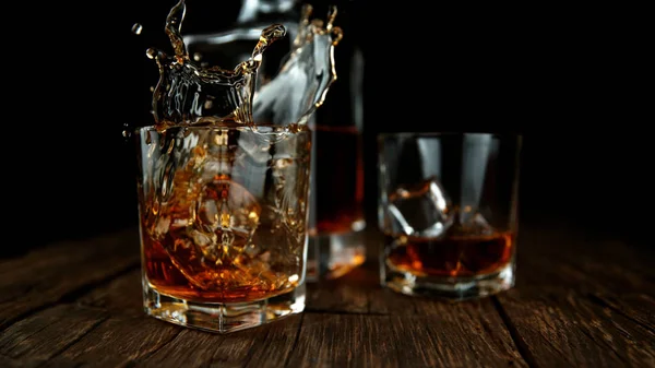 Splashing whiskey from glass with ice cubes inside — Stock Photo, Image