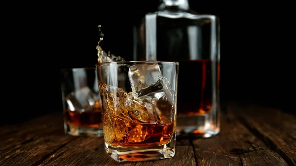 Splashing whiskey from glass with ice cubes inside — Stock Photo, Image