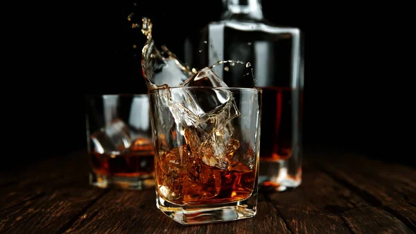 Splashing whiskey from glass with ice cubes inside — Stock Photo, Image