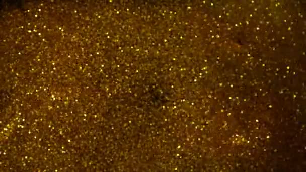 Mouvement super lent de particules dorées scintillantes sur fond noir. Faible profondeur de mise au point. Filmé sur caméra de cinéma à grande vitesse, 1000 images par seconde.