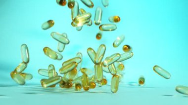 Mavi arka planda düşen altın hapların süper yavaş çekimi. Yüksek hızlı sinema, yavaş çekim kamera, 1000fps.