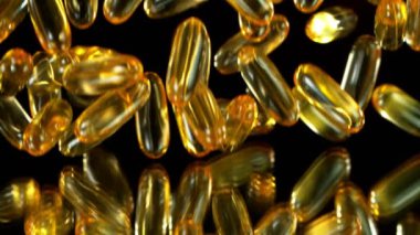 Siyah arka planda düşen altın hapların süper yavaş çekimi. Yüksek hızlı sinema, yavaş çekim kamera, 1000fps.