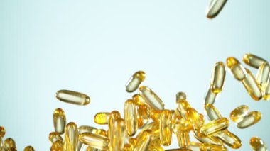 Beyaz arka planda düşen altın hapların süper yavaş çekimi. Yüksek hızlı sinema, yavaş çekim kamera, 1000fps.