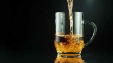 Süper yavaş çekimde siyah arka plana yerleştirilmiş bardağa bira dolduruluyor. Yüksek hızlı sinema kamerası, 1000 fps..