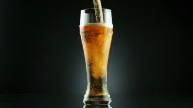 Süper yavaş çekimde siyah arka plana yerleştirilmiş bardağa bira dolduruluyor. Yüksek hızlı sinema kamerası, 1000 fps..