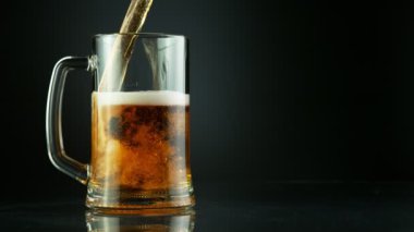 Süper yavaş çekimde siyah arka plana yerleştirilmiş bardağa bira dolduruluyor. Yüksek hızlı sinema kamerası, 1000 fps..