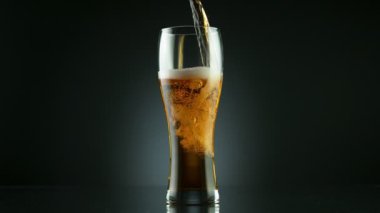 Süper yavaş çekimde siyah arka plana yerleştirilmiş bardağa bira dolduruluyor. Yüksek hızlı sinema kamerası, 1000 fps..