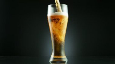 Süper yavaş çekimde siyah arka plana yerleştirilmiş bardağa bira dolduruluyor. Yüksek hızlı sinema kamerası, 1000 fps..