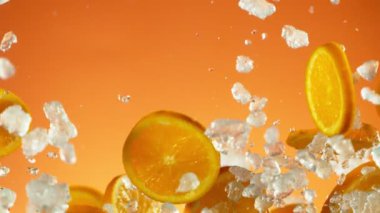 Mavi arka planda ezilmiş buzla birlikte düşen portakal dilimlerinin süper yavaş çekimi. Yüksek hızlı sinema kamerası, 1000 fps..